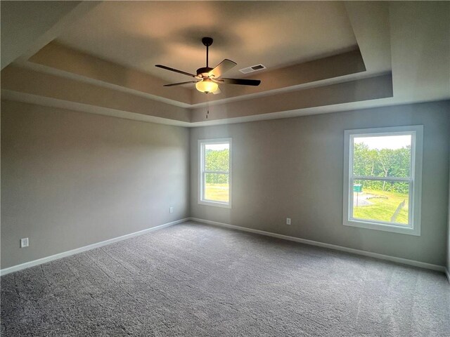 empty room with a raised ceiling, carpet, and ceiling fan