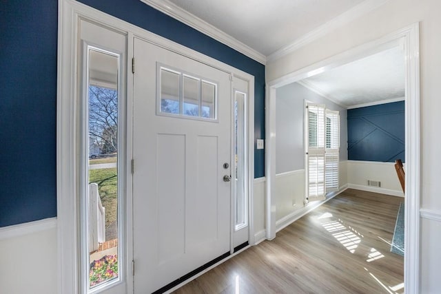 foyer with ornamental molding, wainscoting, visible vents, and light wood-style floors