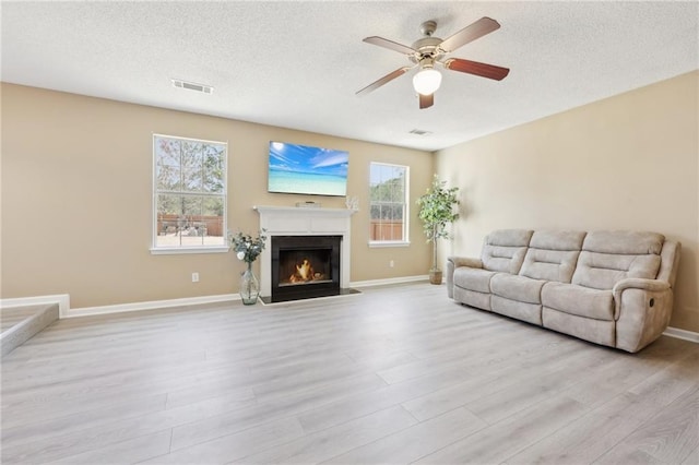 living room with a textured ceiling, a lit fireplace, light wood finished floors, and visible vents