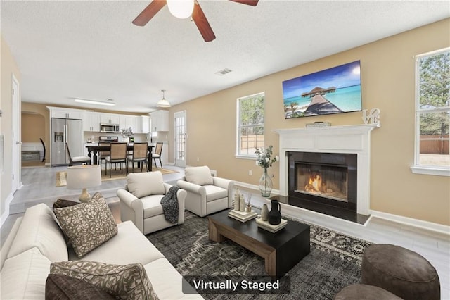 living room with a textured ceiling, a glass covered fireplace, visible vents, and baseboards