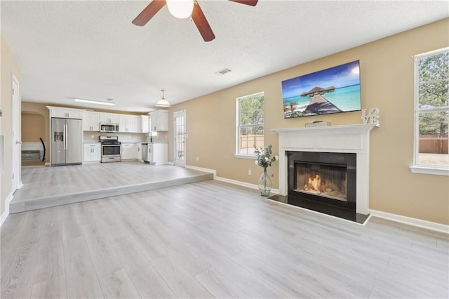 unfurnished living room featuring visible vents, light wood-style flooring, a fireplace with flush hearth, a textured ceiling, and baseboards