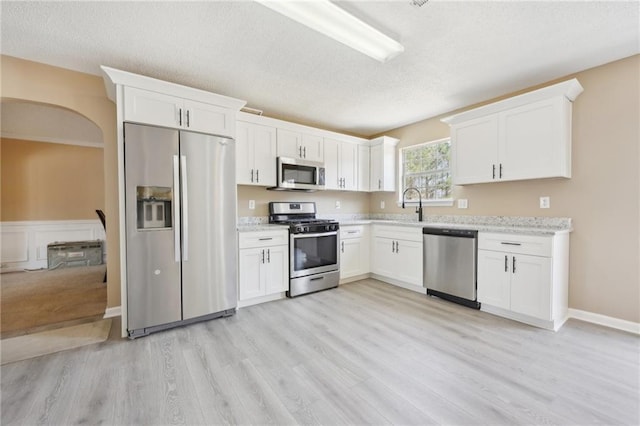 kitchen with appliances with stainless steel finishes, white cabinets, light wood-style floors, and a textured ceiling