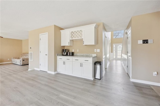 kitchen featuring light wood-style floors, open floor plan, white cabinets, a textured ceiling, and baseboards