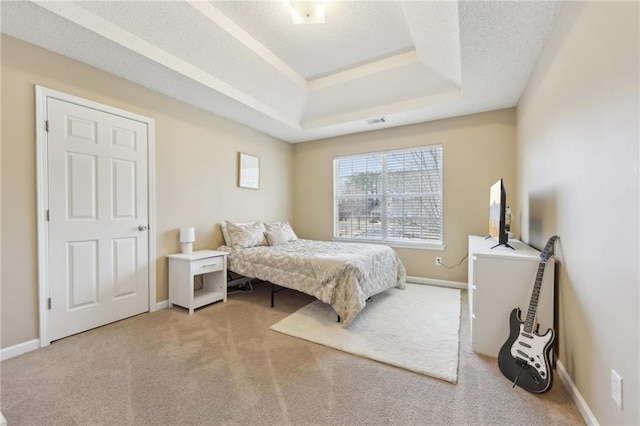 bedroom with a textured ceiling, light carpet, visible vents, baseboards, and a tray ceiling