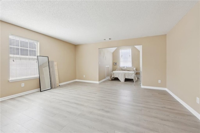 unfurnished bedroom with light wood-style flooring, visible vents, baseboards, and a textured ceiling