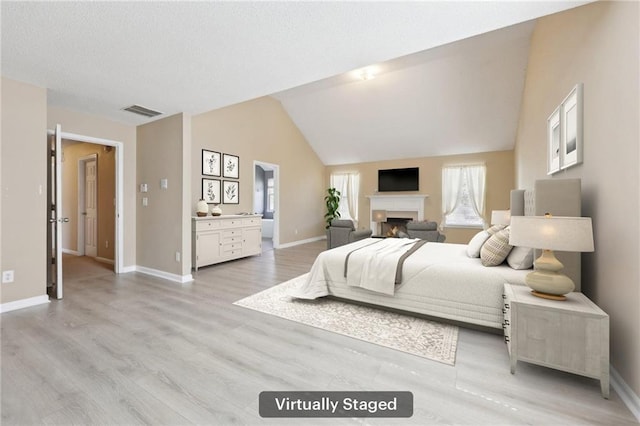 bedroom with a fireplace, visible vents, baseboards, vaulted ceiling, and light wood-style floors