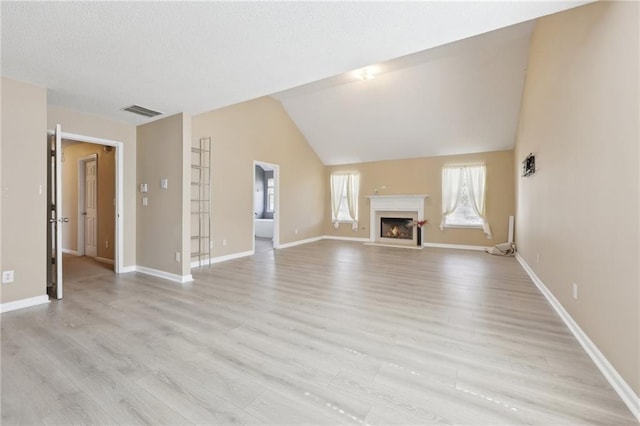 unfurnished living room with visible vents, a fireplace with raised hearth, light wood-style floors, vaulted ceiling, and baseboards