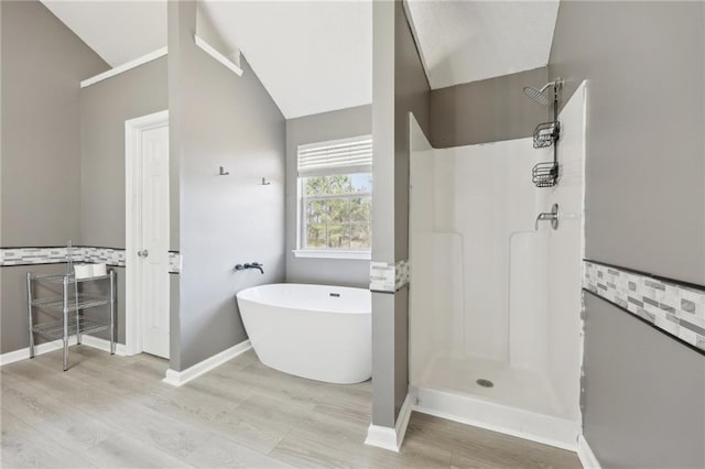 bathroom featuring vaulted ceiling, wood finished floors, a freestanding tub, baseboards, and walk in shower