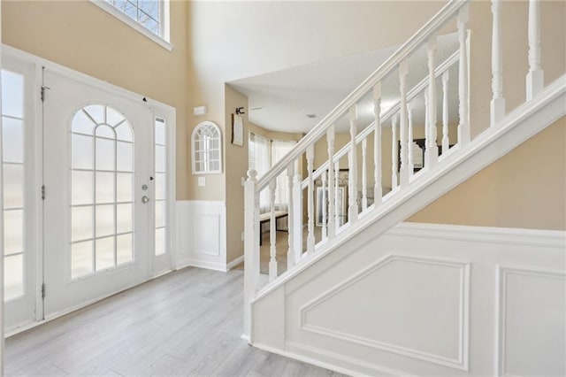 foyer with wainscoting, a towering ceiling, wood finished floors, stairs, and a decorative wall