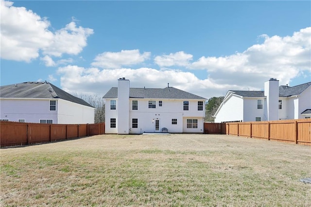 back of property with a fenced backyard, a yard, and a chimney