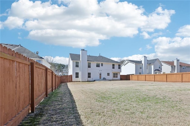 back of property with a yard, a chimney, and a fenced backyard