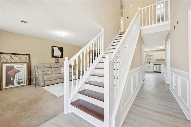 stairs with a decorative wall, a wainscoted wall, carpet floors, wood finished floors, and visible vents