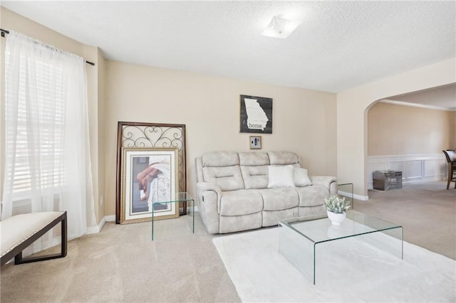 living area with arched walkways, a textured ceiling, and carpet