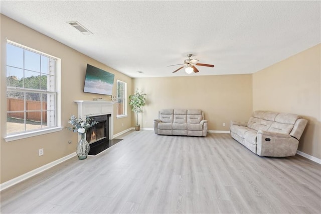 living room featuring a textured ceiling, a glass covered fireplace, wood finished floors, and visible vents