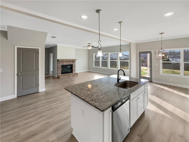 kitchen with a sink, white cabinets, stainless steel dishwasher, a brick fireplace, and dark stone countertops