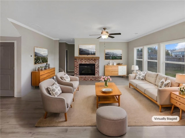 living area with a ceiling fan, a fireplace, ornamental molding, and wood finished floors