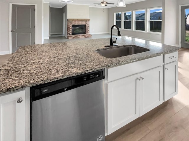kitchen featuring stone countertops, dishwasher, open floor plan, a brick fireplace, and a sink