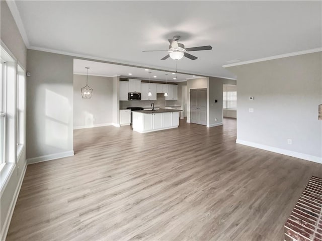 unfurnished living room featuring baseboards, ornamental molding, wood finished floors, a healthy amount of sunlight, and ceiling fan with notable chandelier