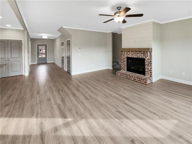 unfurnished living room featuring a brick fireplace, baseboards, ornamental molding, and wood finished floors