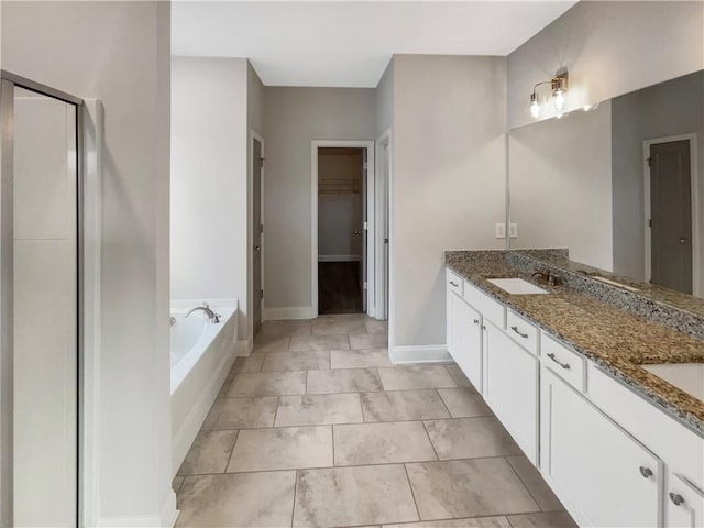 full bathroom featuring double vanity, baseboards, a garden tub, a walk in closet, and a sink
