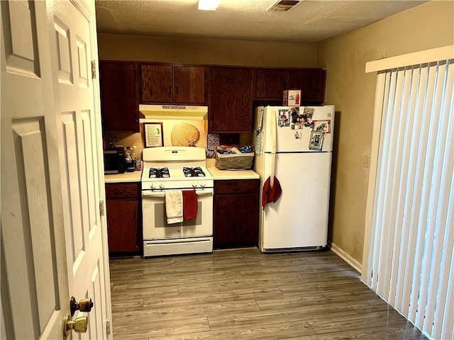 kitchen with white appliances, a textured ceiling, and light wood-type flooring