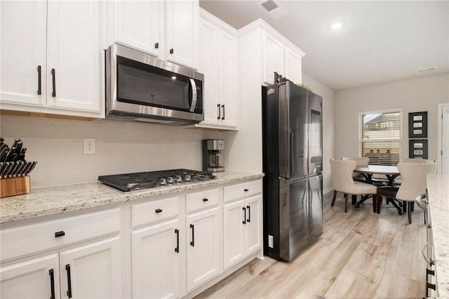 kitchen featuring appliances with stainless steel finishes, light wood-type flooring, light stone countertops, and white cabinets