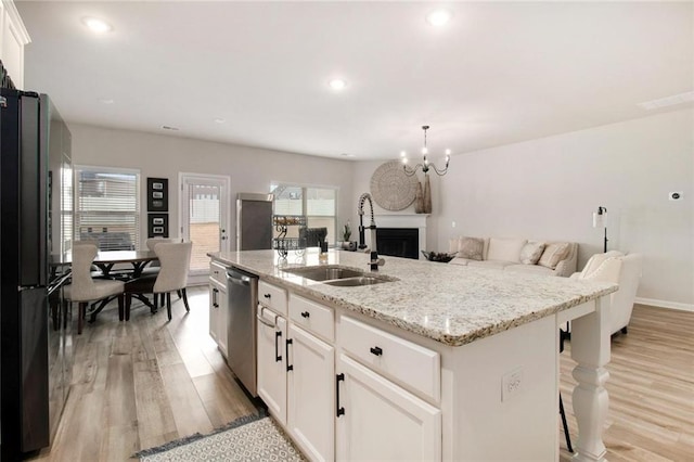 kitchen featuring dishwasher, open floor plan, freestanding refrigerator, a kitchen island with sink, and a sink