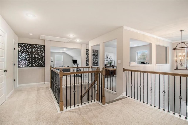 hall with attic access, carpet, crown molding, an upstairs landing, and a chandelier