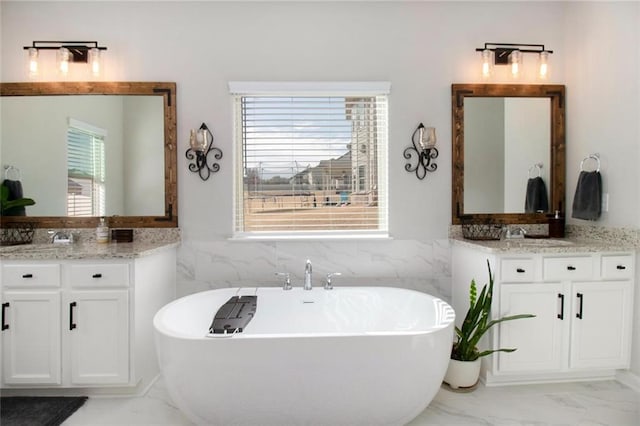 bathroom featuring marble finish floor, two vanities, and a freestanding tub