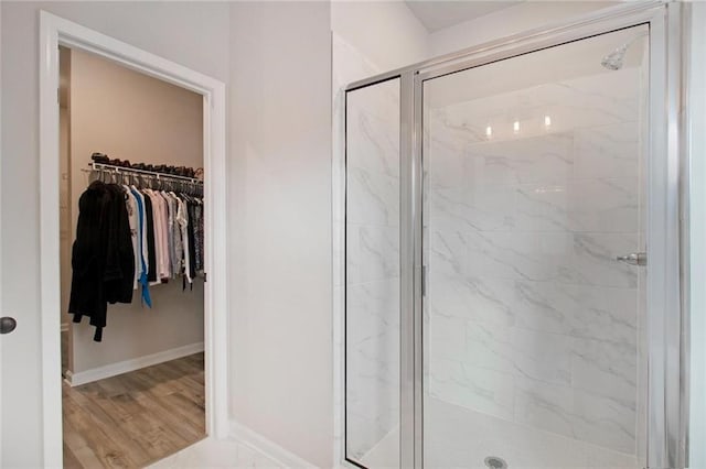 full bath with a walk in closet, baseboards, a marble finish shower, and wood finished floors