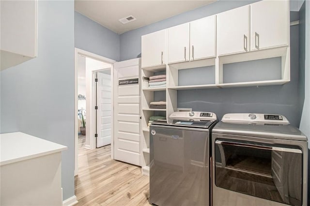 clothes washing area with cabinet space, light wood-style flooring, visible vents, and washer and dryer