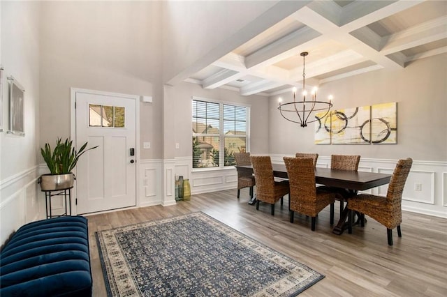 dining area featuring light wood finished floors, wainscoting, a chandelier, a decorative wall, and beam ceiling