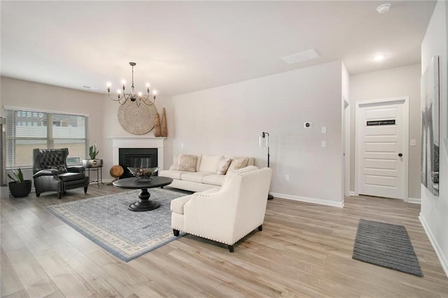 living area featuring a chandelier, a glass covered fireplace, baseboards, and light wood finished floors