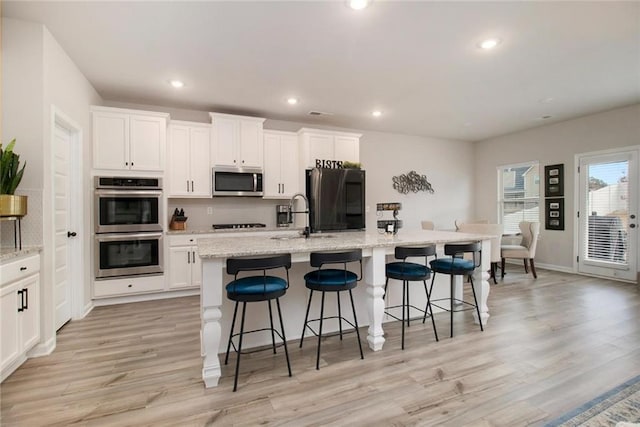 kitchen with light wood finished floors, white cabinets, appliances with stainless steel finishes, a kitchen island with sink, and recessed lighting