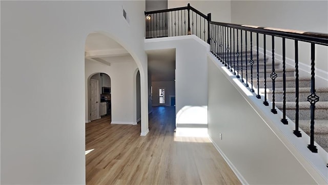 interior space with arched walkways, baseboards, a high ceiling, and wood finished floors