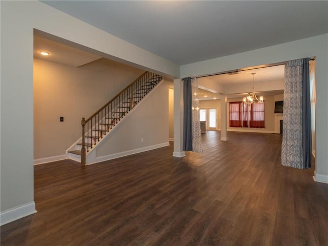 unfurnished living room featuring dark wood-type flooring, a chandelier, and ornate columns