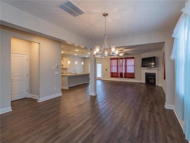 unfurnished living room featuring ceiling fan with notable chandelier and dark hardwood / wood-style floors