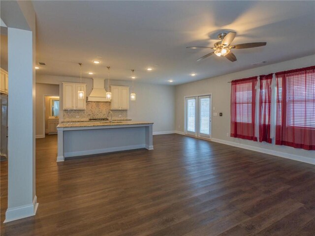 kitchen with white cabinetry, backsplash, custom exhaust hood, hanging light fixtures, and a kitchen island with sink