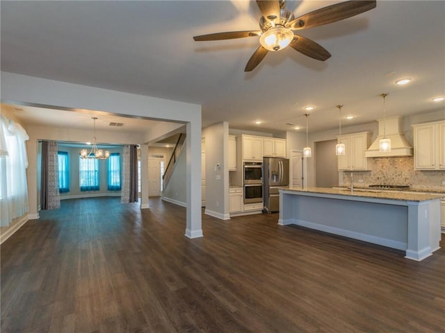 kitchen with custom exhaust hood, decorative light fixtures, appliances with stainless steel finishes, a kitchen island with sink, and white cabinets