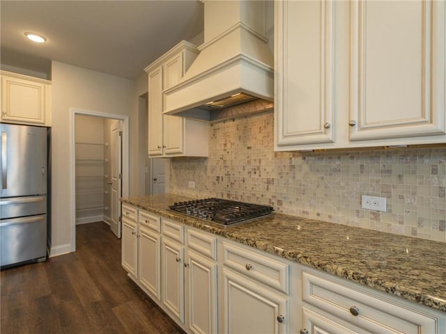 kitchen with premium range hood, tasteful backsplash, light stone counters, stainless steel appliances, and dark wood-type flooring