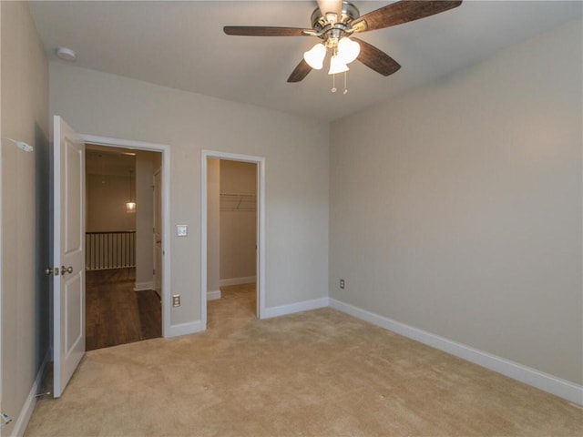 unfurnished bedroom featuring ceiling fan, light colored carpet, a spacious closet, and a closet