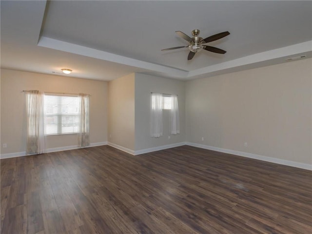 empty room with dark wood-type flooring, ceiling fan, and a tray ceiling