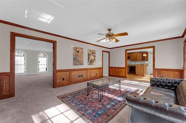 carpeted living room featuring wooden walls, ceiling fan, and crown molding