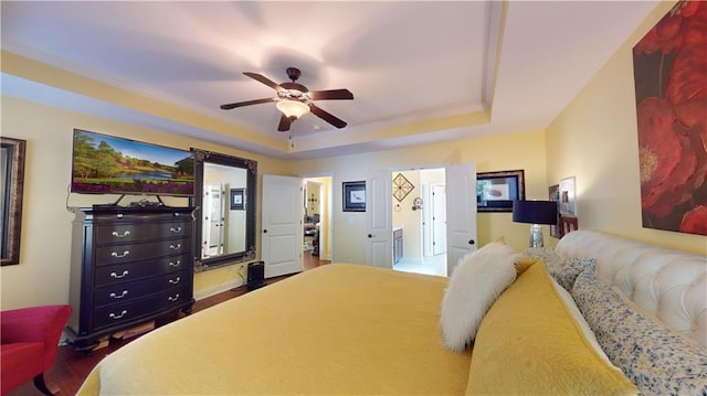 bedroom with ceiling fan, ensuite bathroom, and a tray ceiling