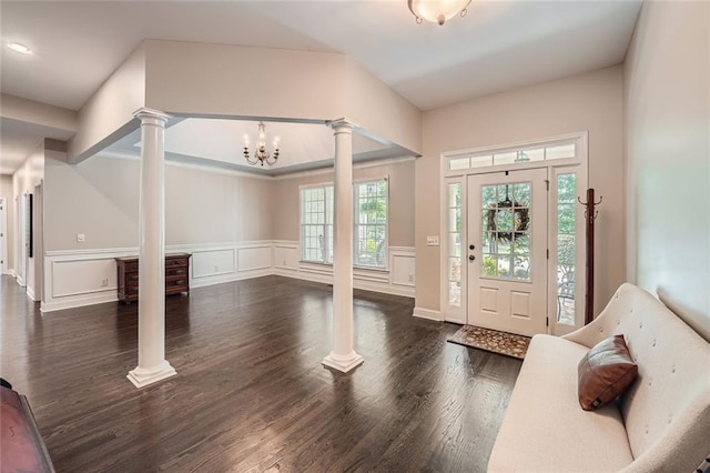 foyer entrance with dark wood-style floors, ornate columns, wainscoting, a decorative wall, and a notable chandelier