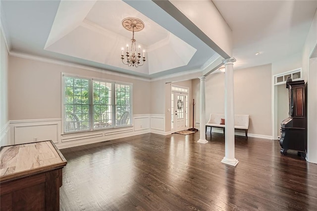 unfurnished living room featuring decorative columns, an inviting chandelier, wood finished floors, a decorative wall, and a raised ceiling