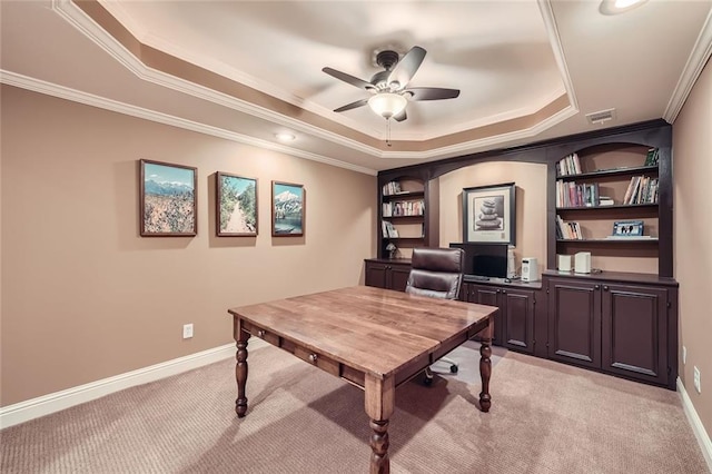 office space featuring a tray ceiling, crown molding, baseboards, light colored carpet, and ceiling fan