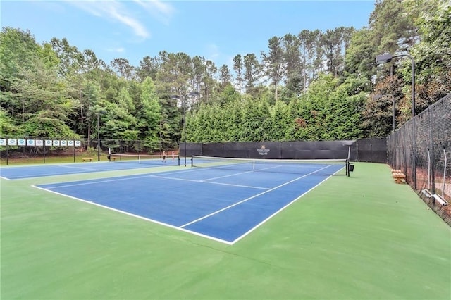 view of tennis court with community basketball court and fence