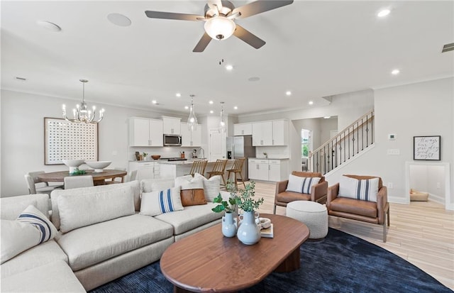 living room with ceiling fan with notable chandelier, ornamental molding, and light hardwood / wood-style flooring