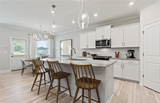 kitchen featuring light stone countertops, electric range oven, white cabinets, and an island with sink